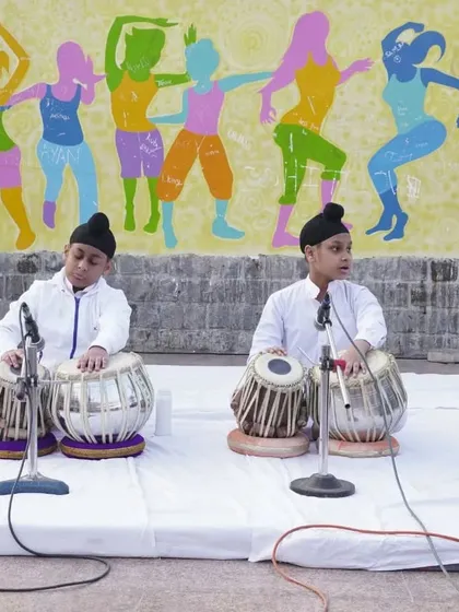 A focused shot of two young students playing tabla in unison during a public performance.