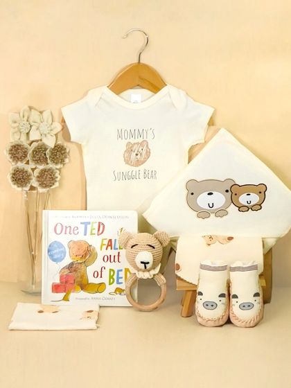 A 'Mommy's Snuggle Bear' gift set arranged outside the box. This allows customers to see each item clearly, including the onesie, book, and rattle.