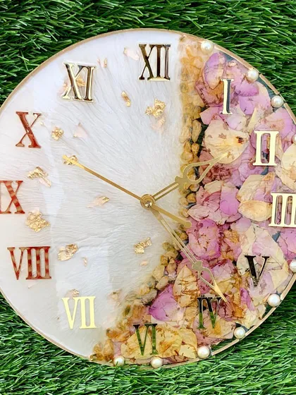 A beautiful varmala preservation clock. The right side features preserved pink and yellow flowers, while the left side has a clean white finish with gold foil.