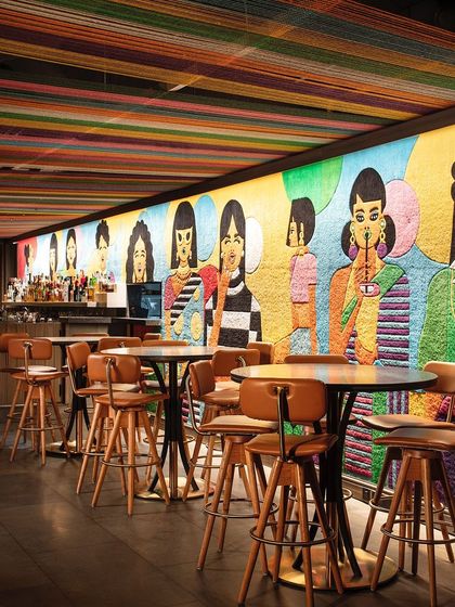Khi Khi, named for the Hindi word for giggles, is a contemporary bar that creates a mirthful, whimsical world. This wide shot shows the stunning bespoke carpet that runs along the wall, creating a vibrant and playful ambiance.