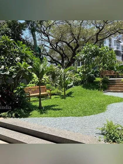 A gravel path winds up a gentle slope, with stone steps providing access to a higher level. A wooden bench is nestled under a mature tree, offering a resting spot along the way.