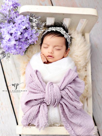 A baby wrapped in a purple bow, sleeping soundly in a miniature white bed.