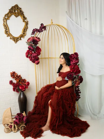 For a touch of glamour, I use setups like my golden birdcage chair, adorned with rich, deep red flowers. This portrait showcases a bold and elegant style, celebrating the mother-to-be in a truly regal way.