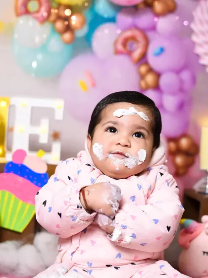 A quiet moment amidst the cake-smashing fun. Even with frosting on her face, her sweet and curious expression shines through in this first birthday photo.
