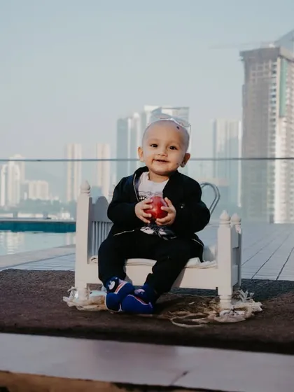 A sweet portrait of a baby boy holding a small apple, sitting on his prop bed by the pool with the city behind him.