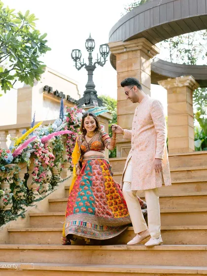 The couple holds hands as they descend a grand staircase, making a beautiful entrance to their Mehendi ceremony.
