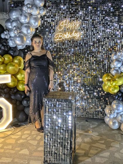 A full view of the birthday girl with the complete setup, including the sequin wall, balloon garland, and a large marquee number.