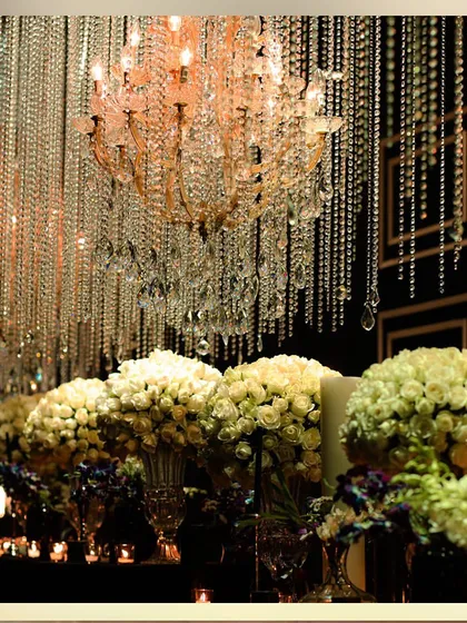 A long bar or buffet table lined with white rose bouquets and candles, under a ceiling of hanging crystals. This creates a stunning visual display.