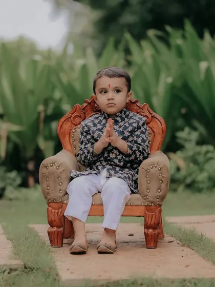 A sweet 'namaste' from this little one. This pose, combined with his traditional attire, makes for a respectful and heartwarming portrait during his outdoor baby shoot.