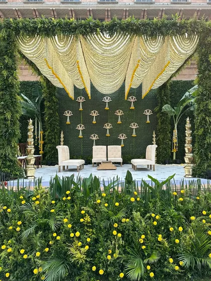 A South Indian-inspired mandap design with a canopy of jasmine flower curtains and a backdrop of woven banana leaves and lotus motifs.