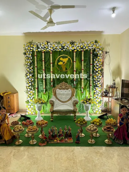 For a more natural and serene theme, I create backdrops using fresh banana leaves. This setup, perfect for an intimate baby shower at home, features hanging jasmine garlands and a classic white and gold throne, complemented by a full arrangement of ceremonial plates.