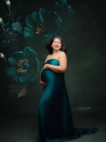 A fine art portrait in a teal gown against a dark, floral-painted backdrop. The mother's serene expression adds to the artistic quality of the shot.