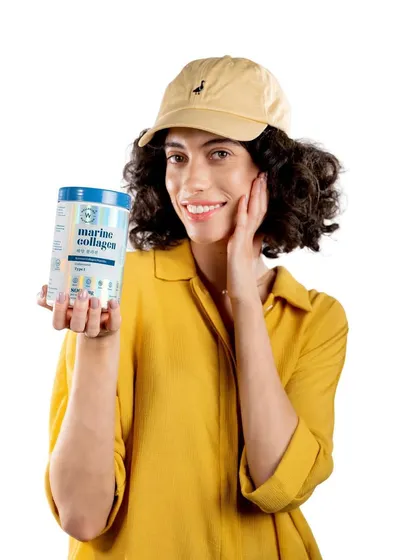 A bright, cheerful lifestyle shot for the Wellbeing Nutrition campaign. The model's happy expression and casual styling make the product feel accessible and part of a healthy, active life.