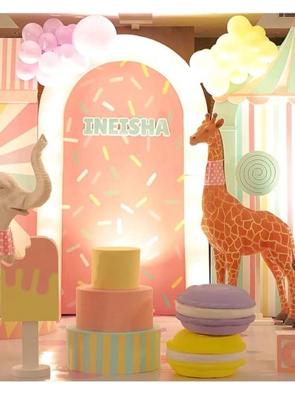 A close-up of the candyland setup, with a tall giraffe prop, a tiered cake, and a giant macaron, all in soft pastel colors.