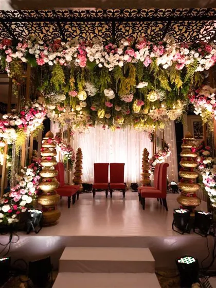This indoor mandap features a ceiling completely covered in hanging flowers and greenery, creating an enchanting forest-like atmosphere for the wedding ceremony.