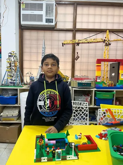 A glimpse into our vibrant learning center where ideas take shape. This student stands with his completed project in a classroom filled with inspiring, large-scale LEGO models like a crane and Ferris wheel, showcasing the exciting possibilities that await.