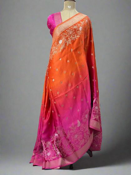 A vibrant shaded satin saree transitioning from orange to pink with a delicate floral border.