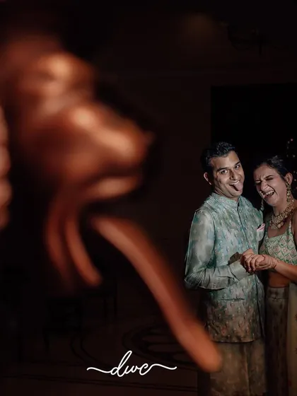 A fun and candid moment captured during a Roka ceremony, with the couple sharing a laugh, playfully framed by a foreground object.