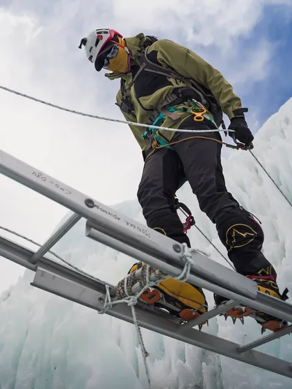 A climber practices crossing a ladder over a deep crevasse in the Khumbu Icefall. This essential skill is practiced extensively at base camp to build confidence for the journey ahead.
