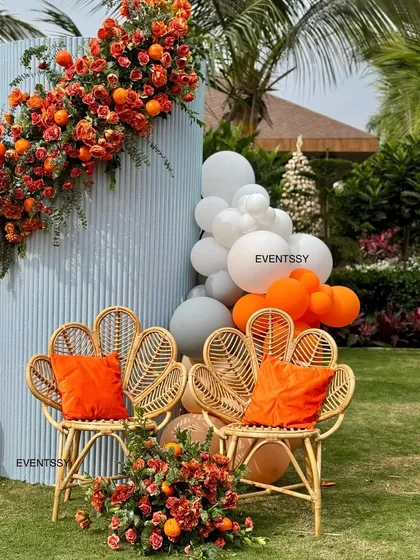 A detail shot of the custom wicker chairs and floral arrangements from the "Tangerine & Twinkles" baby shower. The combination of fresh flowers, real oranges, and natural textures creates a unique and stylish photo corner.