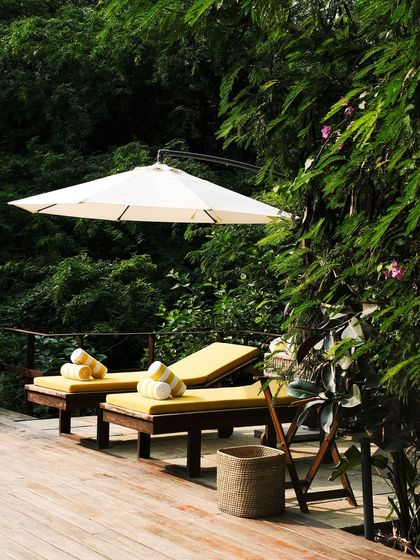 The cantilevered umbrella provides shade for the loungers, nestled amongst the dense foliage at the edge of the pool deck.