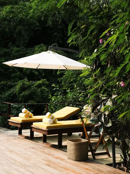 The cantilevered umbrella provides shade for the loungers, nestled amongst the dense foliage at the edge of the pool deck.