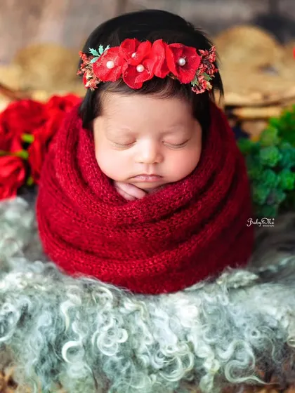 Wrapped snugly in a bold red knit, this newborn looks so cozy and content. The color contrast with the floral headband makes the image pop.
