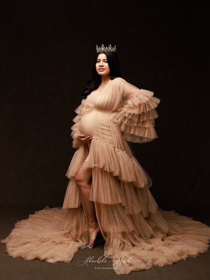 A regal portrait in a crowned, nude-toned gown, showcasing a confident and elegant pose against a classic dark backdrop.