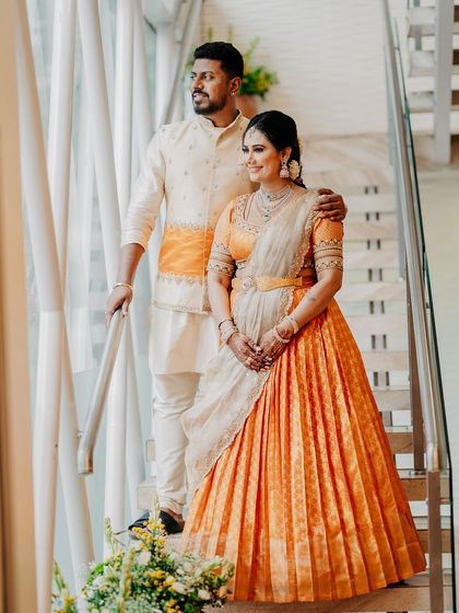 A wide shot of the couple on the stairs, looking out a window. Their coordinated orange and cream outfits stand out beautifully.