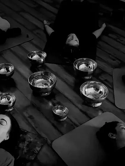 A black and white photo capturing the deep relaxation of a sound healing session, with singing bowls placed around the students.