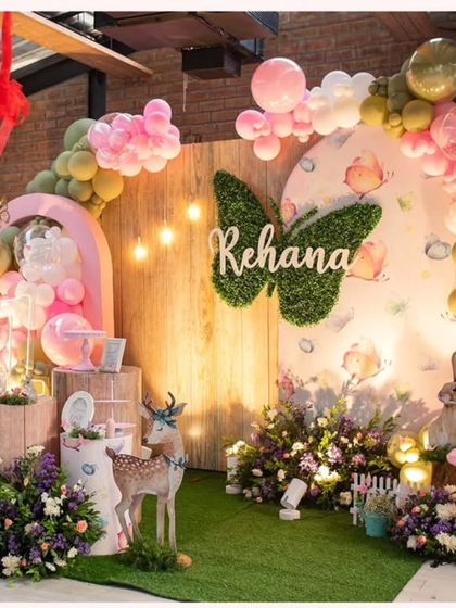 An enchanted woodland birthday theme for Rehana. The decor features a moss butterfly with the name, a gentle deer prop, and a mix of florals and balloons in a rustic setting.