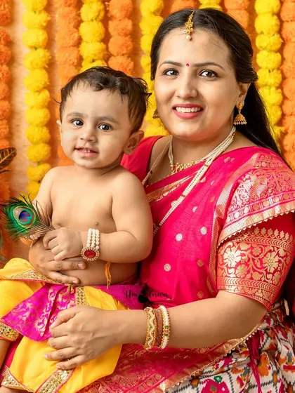 A mother holds her little one, who is holding a peacock feather, a symbol of Lord Krishna. A tender and symbolic portrait.