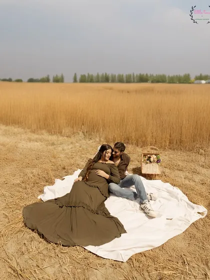 A wide shot of the couple enjoying a quiet moment together in the field, a perfect scene for their pregnancy announcement.