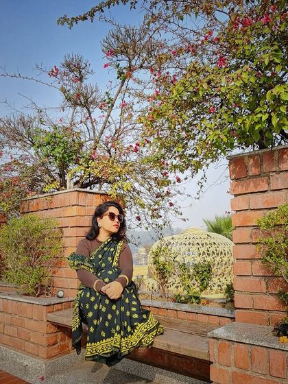 A pensive moment in a beautiful printed saree, set against a backdrop of nature and architecture.