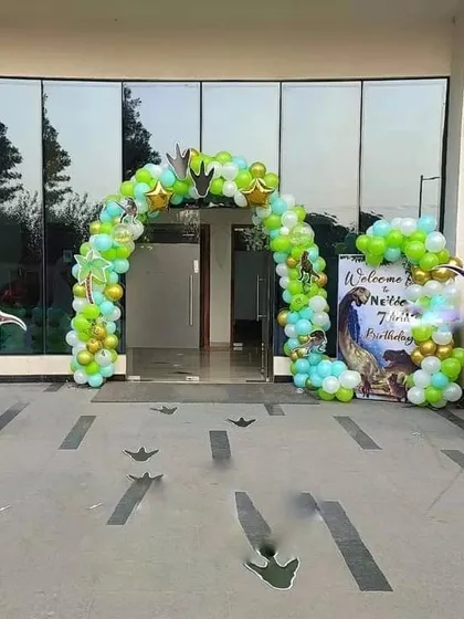 A dinosaur-themed party entrance in a backyard. This setup includes a balloon arch, a welcome sign, and dinosaur cutouts with footprints leading the way.