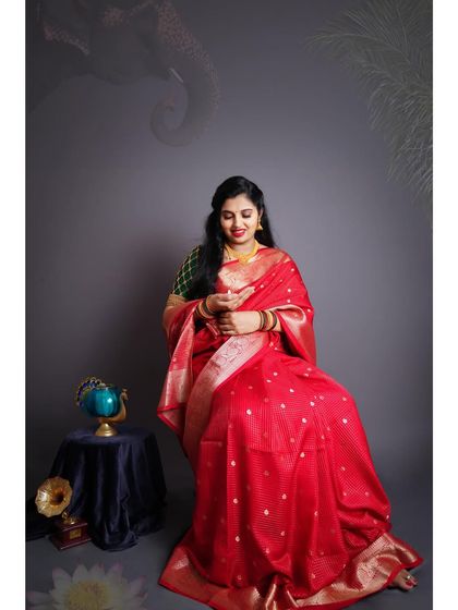 A beautiful indoor traditional maternity portrait. The mother-to-be is seated, glowing in a red saree, with artistic props like a globe and gramophone.