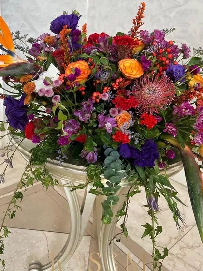 A riot of colour and texture. This arrangement is a symphony of Dutch berries, African Pincushion, Lisianthus, and Roses. The out-of-the-box colour combination of oranges, purples, and reds makes for a truly striking centerpiece.