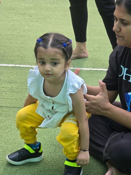 Look at that focus! A coach provides gentle support as a young girl practices her squat form. We work on fundamental movements from an early age to build a strong foundation for lifelong fitness.