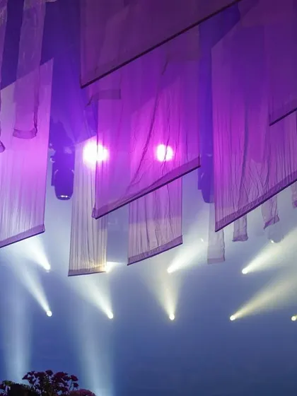An abstract ceiling view from an evening event at the same location, where beams of light cut through hanging white fabrics, creating a dramatic and modern effect.