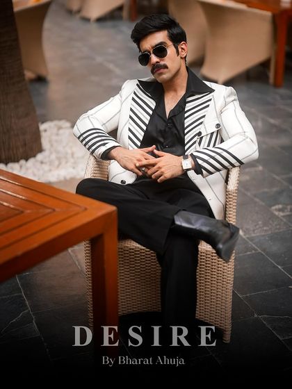 Seated with an air of authority, this image shows the white pinstripe blazer paired with black trousers and boots, creating a look of retro-inspired power.
