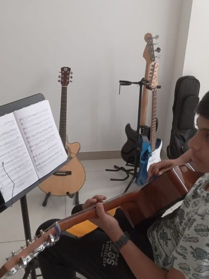 A student practicing his guitar chords, with other instruments in the background.