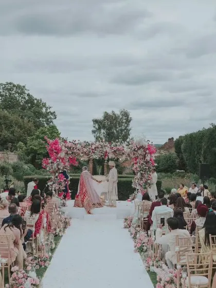 The full view of the outdoor wedding ceremony in a manicured English garden. This shot captures the beautiful setup, the guests, and the grandeur of the estate.
