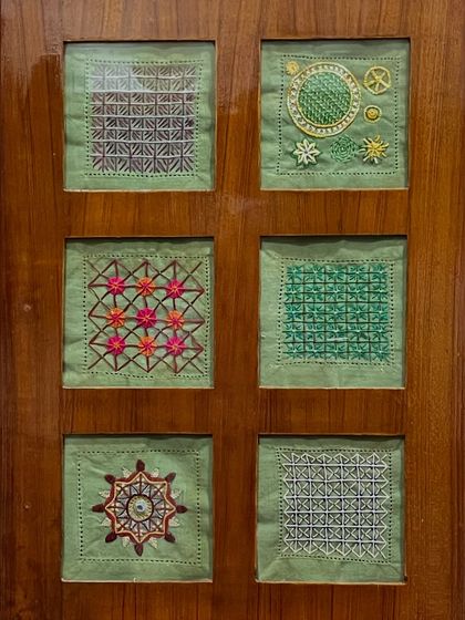 Another set of framed embroidery samplers, this time on a green background. Each square showcases a different stitch or pattern.