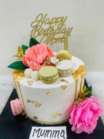 An elegant cake for "Mumma," featuring a white base with a gold drip, topped with beautiful sugar peonies and macarons.