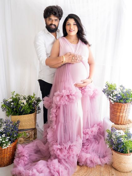 A classic and happy portrait of an expecting couple standing together, surrounded by flowers, looking at the camera.