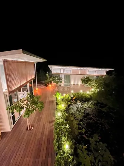 The wooden deck extends over the landscape, with carefully placed lighting to guide the way at night. The glow from the house illuminates the edge of the lily pond, creating a serene and romantic setting.