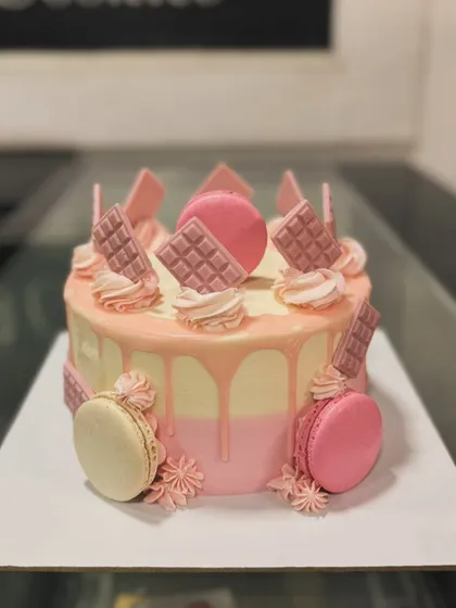 A pink drip cake decorated with macarons and ruby chocolate bars.