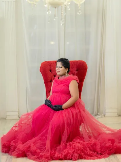 An elegant, regal portrait of a mom-to-be seated in a throne-like chair, wearing a beautiful red gown and gloves.
