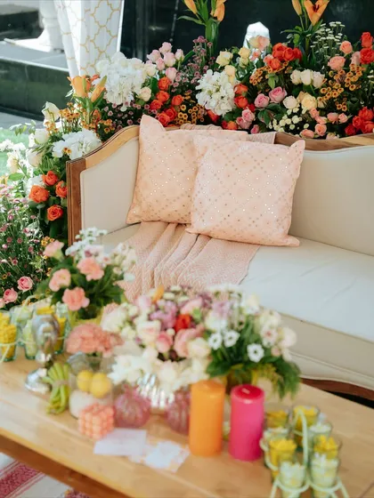 A comfortable and stylish seating area for the 'Nazar na lage' lunch, with a sofa surrounded by a profusion of colorful flowers. The pastel cushions add a soft, welcoming touch.