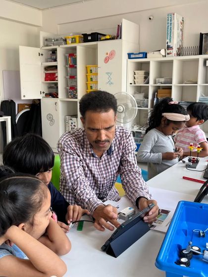 Our instructors provide personalized guidance to ensure every child understands the concepts. Here, a group of curious students gathers around a tablet to learn a new programming skill during our summer camp.